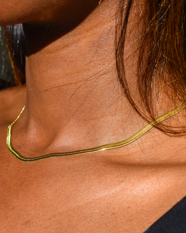 woman wearing waterproof 3mm best selling herringbone necklace in gold with a black top and brown hair