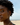 woman looking into the camera at the beach. she has curly hair and two gold hoop earrings with 2 gold ear cuffs 