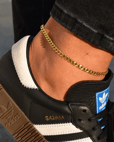 waterproof gold curb chain anklet shown on an ankle with black jeans and black adidas samba sneakers. 